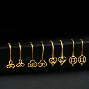 May include: A collection of gold-colored dangle earrings with various designs, including floral, cloud, heart, and coin shapes. The earrings are displayed against a dark background, showcasing their intricate details and shine.