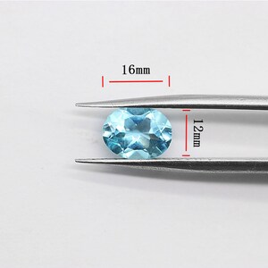 May include: A light blue oval gemstone measuring 16mm by 12mm. The gemstone is held in place by a pair of tweezers.