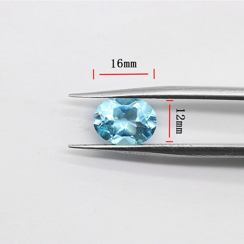 May include: A light blue oval gemstone measuring 16mm by 12mm. The gemstone is held in place by a pair of tweezers.