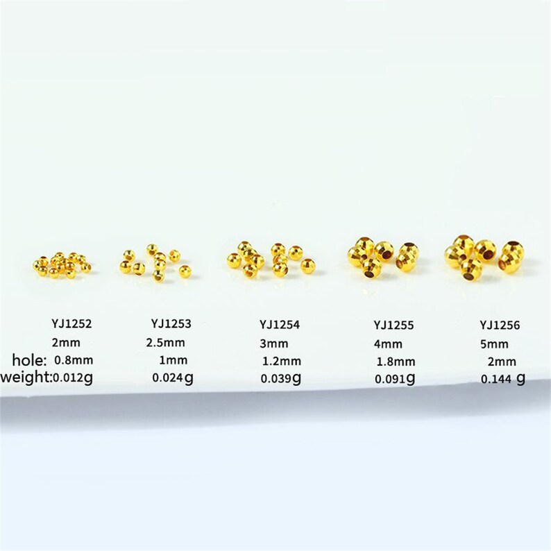 May include: Five rows of gold-colored metal beads of varying sizes, with the bead size increasing from left to right. Each row is labeled with a product code, size in millimeters, hole size in millimeters, and weight in grams.