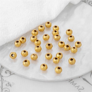 May include: A collection of small, round, gold-colored beads, each featuring a textured, woven-like surface pattern and a central hole. These metallic beads are scattered across the surface, displaying a consistent spherical shape and finish.