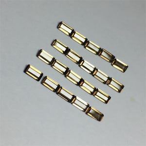 May include: A row of five gold and clear rectangular gemstones, each with a faceted design. The gemstones are arranged in a staggered pattern, with the top row having the most gemstones and the bottom row having the fewest. The gemstones are all the same size and shape.