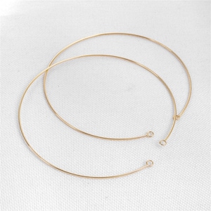 Pode incluir: Duas gargantilhas de metal dourado. Cada colar é um fio fino e circular com pequenas argolas nas extremidades. Os colares são exibidos em uma superfície branca.