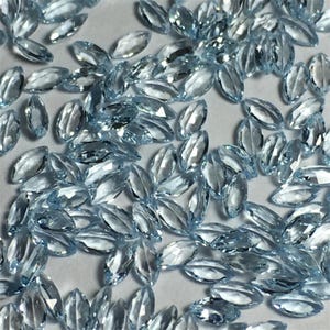 May include: A collection of light blue marquise-shaped gemstones. The gemstones are faceted and have a clear, glassy appearance.