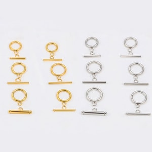 May include: An assortment of toggle clasps in gold and silver tones. Each clasp features a circular ring connected to a straight bar. The clasps are arranged in rows, showcasing their design and finish. Ideal for jewelry making.