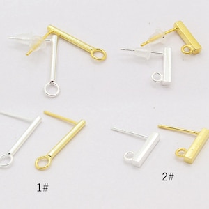 May include: A collection of metal earring posts featuring a horizontal bar design with a small circular loop at one end. The set includes both gold-tone and silver-tone finishes, each paired with clear plastic earring backs for secure fastening.