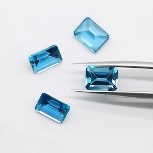 May include: Four blue topaz gemstones in emerald cut, with one held by tweezers.