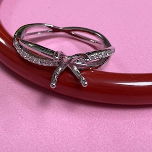 May include: A silver ring with a prong setting for a centre stone. The band is twisted and has small diamonds set in it.