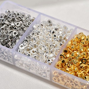 May include: A clear plastic container with three compartments filled with small silver and gold metal jump rings. The jump rings are in various sizes and are perfect for jewellery making.