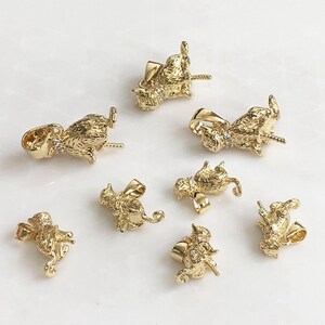 May include: A collection of eight gold-toned metal cat-shaped pendants, each featuring a textured surface and a small clear stone set at the collar. Each pendant includes a bail at the top for attachment, showcasing a detailed feline design.