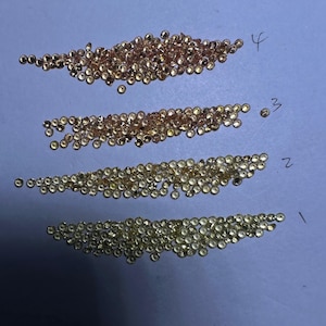 May include: Four horizontal rows of small, round, faceted gemstones arranged by color gradient. The top row is a deep copper-orange, the second is a lighter peach, the third is a pale gold, and the bottom row is a bright yellow. Each row is labeled 1-4.