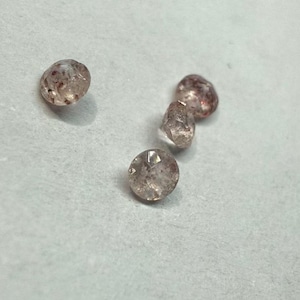 May include: Five small, faceted, clear, round gemstones with red and brown inclusions. The gemstones are arranged in a loose cluster on a white surface.