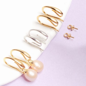 May include: An assortment of earrings in gold and silver tones. The earrings include ear cuffs and drop earrings with pink pearls. The earrings are displayed on a white surface against a light purple background.