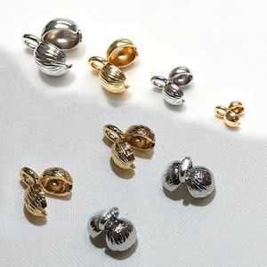 May include: A collection of metallic bead tips or clamshell knot covers in various sizes and finishes, including polished gold and silver tones. Each piece features a textured, rounded shell-like design with a small loop at the top for attachment.