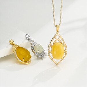 May include: Three pendants featuring smooth, oval-shaped gemstones in yellow and pale green. The pendants are set in gold and silver-toned metal frames accented with small, clear stones. One gold pendant hangs from a matching chain.