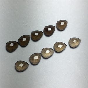 以下が含まれることがあります： 10個のファセットカットされた涙型の煙水晶。石は濃い茶色で、わずかに光沢があります。