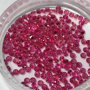 Può includere: Una vista ravvicinata di un contenitore pieno di piccole pietre preziose rotonde di colore rosso. Le pietre preziose sono sparse casualmente in tutto il contenitore.