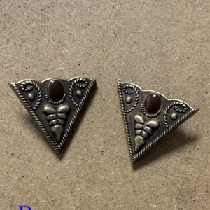 May include: Two gold-tone triangular metal embellishments with a brown stone in the center. Each embellishment has a decorative design around the stone and along the edges.