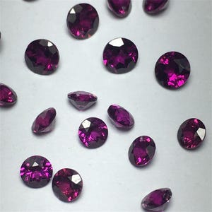 May include: A collection of round, purple gemstones. The gemstones are faceted and have a shiny, polished finish.