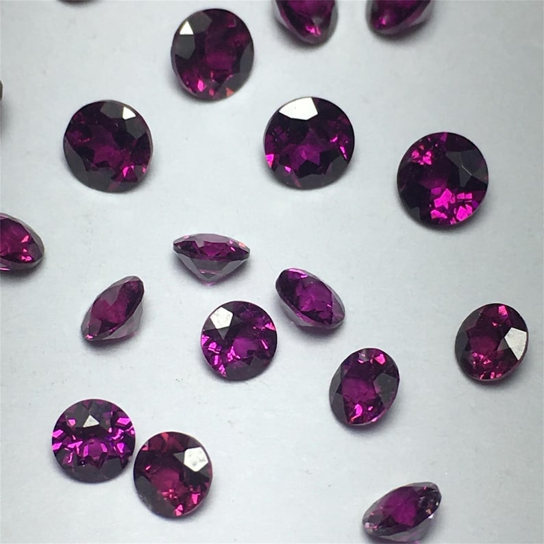 May include: A collection of round, purple gemstones. The gemstones are faceted and have a shiny, polished finish.