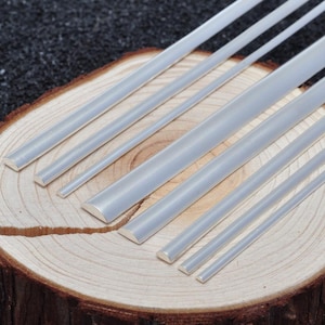 Può includere: Una collezione di sette aste metalliche color argento con sezione trasversale semicircolare, disposte in formazione parallela. Le aste variano in spessore e lunghezza, presentando una superficie liscia e riflettente che cattura la luce.