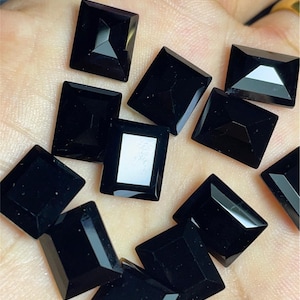 May include: A collection of black square-shaped gemstones, likely onyx, displayed on a hand. The gemstones are faceted and have a polished finish.