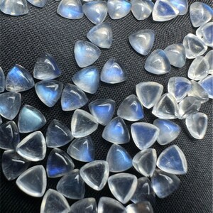 Peut inclure: Une collection de cabochons de pierre de lune blanche irisée de forme triangulaire. Les pierres ont un léger reflet bleu et sont parfaites pour la fabrication de bijoux.