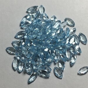 May include: A large pile of light blue marquise-shaped gemstones. The gemstones are faceted and have a glassy finish.