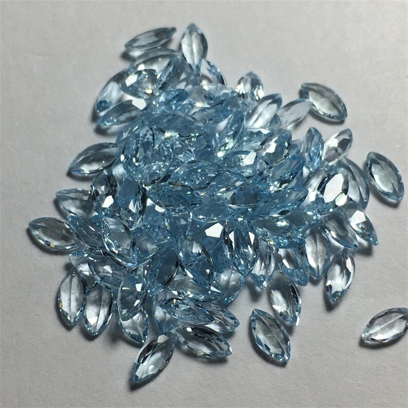 May include: A large pile of light blue marquise-shaped gemstones. The gemstones are faceted and have a glassy finish.