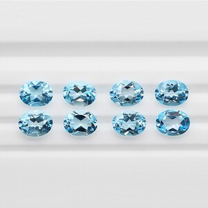 May include: Eight oval-shaped, light blue gemstones on a white background.