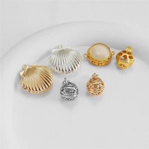 Peut inclure: Un ensemble de six breloques en métal comprenant deux pendentifs coquillages en or et argent, deux perles sphériques en filigrane en argent et or, une breloque circulaire dorée avec un centre blanc lisse et une breloque cage patte.