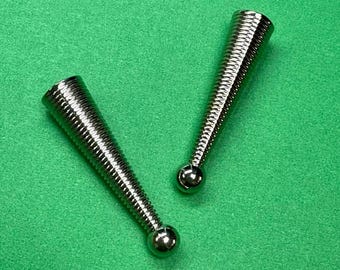 May include: Two silver-colored, conical objects with a spiral design and a small ball at the base. The objects are on a green background. The items appear to be decorative or functional hardware.