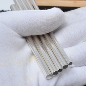 May include: A collection of multiple thin, cylindrical metal rods with a polished, reflective silver-toned finish. The rods are straight, smooth, and uniform in shape, arranged in a parallel bundle, showcasing a bright, metallic luster.