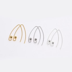Puede incluir: Tres pares de pendientes en oro, plata y un tono plateado más claro. Cada par presenta un diseño de alambre curvado con una pequeña bolita redonda en la parte inferior. Los pendientes se muestran sobre un fondo blanco liso.