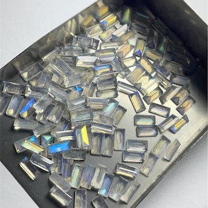 以下が含まれることがあります： 虹色の長方形のファセットカットされた宝石でいっぱいの箱。石は半透明で、虹色の輝きがあります。