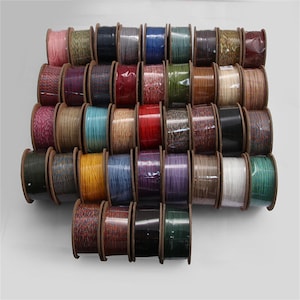 May include: A collection of spools of colorful cord, arranged in rows. The cords are in various colors, including pink, blue, green, and red. The spools are made of wood and are wrapped in clear plastic.