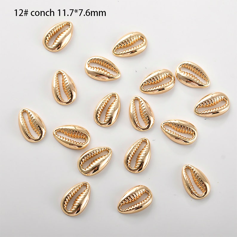 May include: A collection of 18 gold-coloured seashell charms, each measuring 11.7 mm by 7.6 mm. The charms are arranged on a white background.