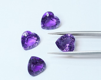 Könnte beinhalten: Vier herzförmige Amethyst-Edelsteine, einer mit einer Pinzette gehalten, auf weißem Hintergrund.
