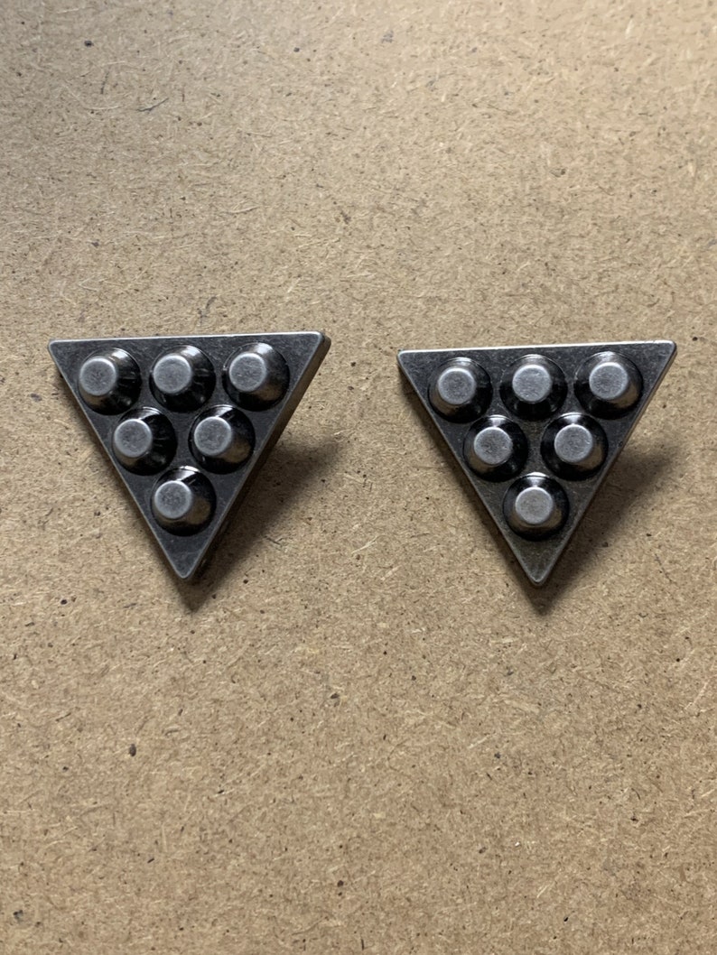 May include: Two silver triangle-shaped metal embellishments with a raised design of seven circles.