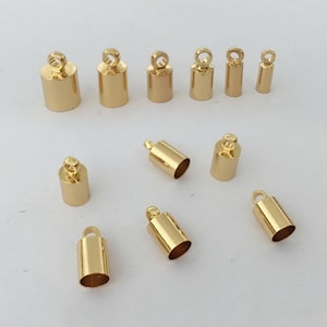 May include: A selection of gold-coloured metal end caps for jewellery making. The caps are cylindrical with a small loop at the top for attaching to chains or cords. Various sizes are shown.