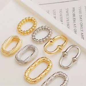May include: An assortment of gold and silver-toned jewelry findings, including oval and circular link connectors. Some have textured surfaces, while others are smooth. The text in the background reads, "JUST FOR TODAY I WILL..."