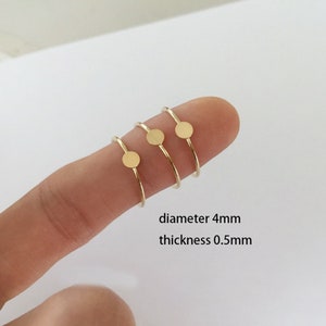 May include: Three gold rings with a 4mm diameter circle on each. The rings are stacked on a finger and the text "diameter 4mm thickness 0.5mm" is below the rings.