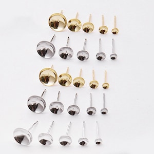 Peut inclure: Une collection de clous d'oreilles en métal avec des coupelles circulaires plates pour la création de bijoux. L'ensemble comprend plusieurs rangées de tiges dorées et argentées, disposées par taille décroissante de gauche à droite.