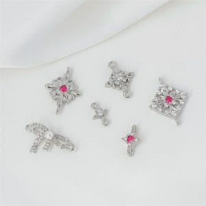 Può includere: Una collezione di sei connettori per gioielli in metallo argentato con pietre di zirconia cubica trasparenti, piccole gemme circolari rosa e una perla bianca. I pezzi presentano forme floreali, a fiocco e geometriche con piccoli anelli.