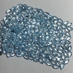 May include: A large pile of light blue marquise-shaped gemstones. The gemstones are faceted and have a brilliant shine.