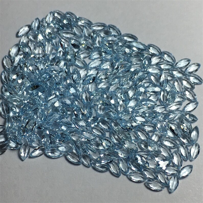 May include: A large pile of light blue marquise-shaped gemstones. The gemstones are faceted and have a brilliant shine.