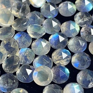 May include: A collection of iridescent, faceted, round, gemstone beads. The beads are a light blue color with a shimmery, iridescent finish.