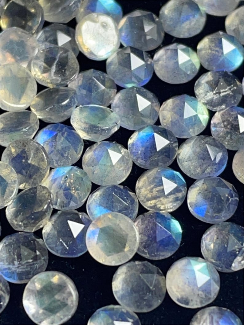 May include: A collection of iridescent, faceted, round, gemstone beads. The beads are a light blue color with a shimmery, iridescent finish.