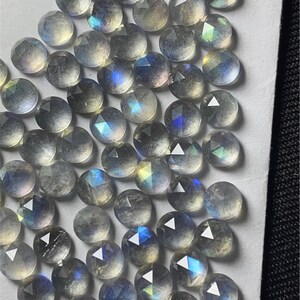 May include: A collection of iridescent, faceted, round labradorite gemstones. The stones are a light gray color with blue and green iridescence.