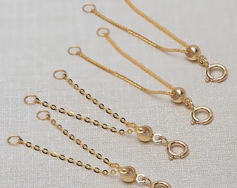 May include: Four gold-colored necklace extenders with a delicate chain design. Each extender features a small, round clasp and a small bead. The extenders are designed to add length to necklaces or bracelets.